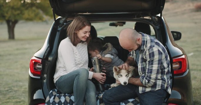 Beautiful family with a small boy and a cute husky dog have trip with car , they have stop in the middle of nature sitting in the trunk of the car and playing toy.