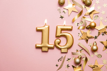 Number 15 gold celebration candle on star and glitter background