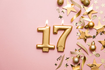 Number 17 gold celebration candle on star and glitter background