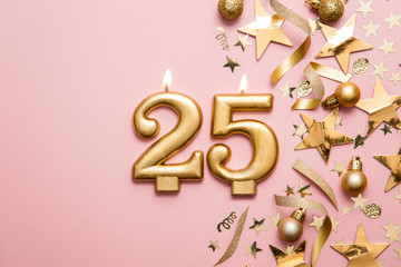 Number 25 gold celebration candle on star and glitter background