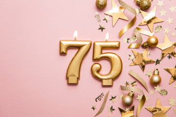 Number 75 gold celebration candle on star and glitter background