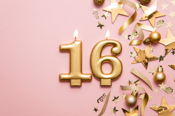 Number 16 gold celebration candle on star and glitter background