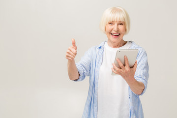 Grey haired old smiling business woman reading browsing using holding tablet. Isolated over white...