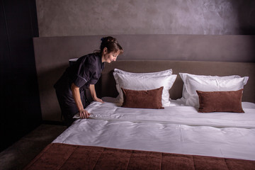 Hotel maid setting up pillow on bed sheet in hotel room