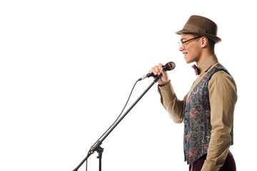 side view of smiling mixed race male musician in hat singing in microphone isolated on white