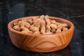 Peanuts in a wood bowl and on marble table