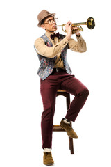 stylish hipster man in hat and eyeglasses playing on trumpet while sitting on chair isolated on...