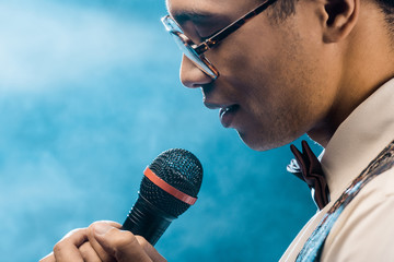 partial view of mixed race man singing in microphone on stage with smoke and dramatic lighting
