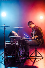 Fototapeta na wymiar male rock star in leather jacket playing drums during concert on stage with smoke and spotlights