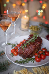 Roast beef and confit tomatoes on the holiday table on the background of Christmas lights