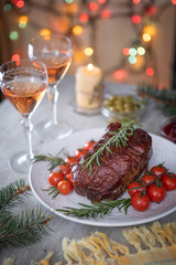 Roast beef and confit tomatoes on the holiday table on the background of Christmas lights
