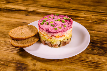 White plate with russian traditional new year salad herring under fur coat and rye bread on wooden table
