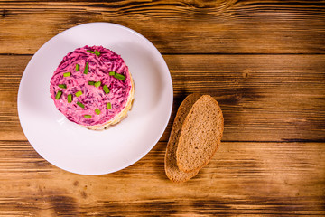 White plate with russian traditional new year salad herring under fur coat and rye bread on wooden table. Top view