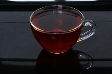 Glass cup of brown tea on black table in cafe