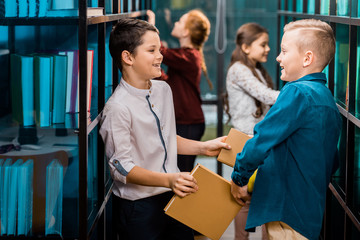 side view of adorable happy schoolkids holding books and smiling each other in library