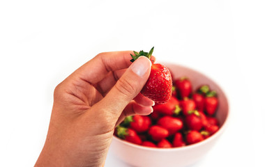 One red strawberry in a hand, close up.  A plate full of strawberries, isolated on white background.