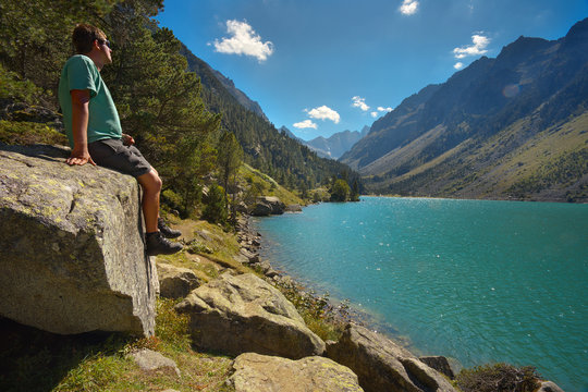 Tourist sitting on the big stone watching a mountain lake Lac de Gaube, Pyrenees Occidentales, France
