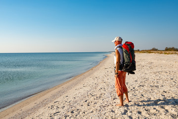 Traveler with backpack stands on the deserted beach