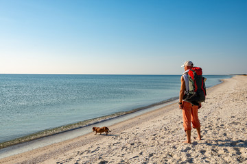 Traveler with funny dog stands on the deserted beach