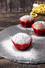 Chocolate muffins on a dark background with a twig decoration painted with icing sugar