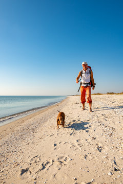 Joyful traveler with funny dog goes along the deserted beach
