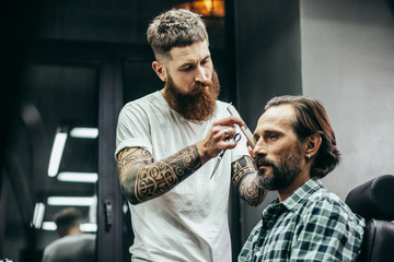 Calm bearded barber standing next to the client and holding comb