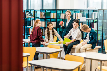 adorable schoolchildren and young female librarian standing and sitting in library