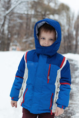 Little boy in a blue winter jacket on the street with snow.