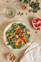 Top view on a vegetarian salad which is made from raw vegetables such a persimmon, kale, pomegranate seeds and walnut. Healthy food and lifestyle concept, flat lay.