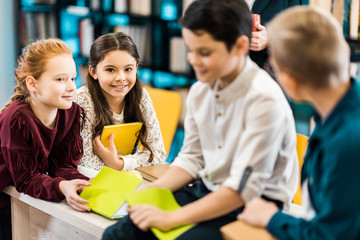 adorable smiling schoolchildren with books sitting together in library
