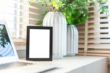Blank black color picture frame template for place image or text inside on the desktop table work space with laptop and flower. window light
