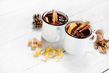 Hot mulled wine in white rustic mugs with spices and citrus fruit on wooden surface. Space for...