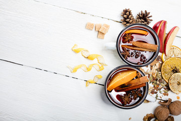 Hot mulled wine in white rustic mugs with spices and citrus fruit on wooden surface. Space for...