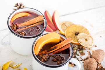 Hot mulled wine in white rustic mugs with spices and citrus fruit on wooden surface. Space for...