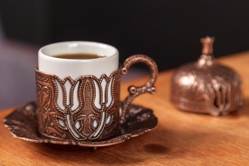 Richly decorated small traditional Turkish Cup for strong black coffee on wooden background. The concept of coffee for the cafe. Turkish coffee in a metal embossed copper Cup on a wooden table.