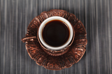 Richly decorated small traditional Turkish embossed copper Cup for strong black coffee on grey background top view, close-up. The concept of coffee for the cafe.