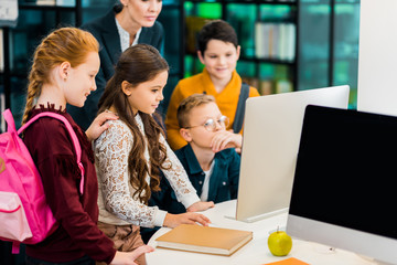 cute schoolkids and librarian using computer together in library