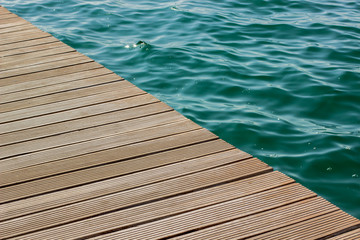 wooden deck floor background texture diagonal line and vivid blue and green water with small waves on a surface in big swimming pool, copy space pattern