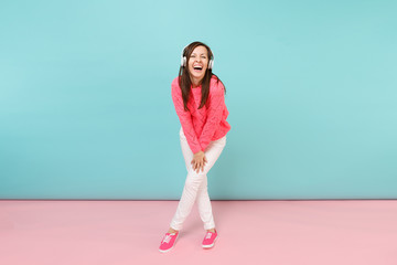 Full length portrait of happy young woman in knitted rose sweater, white pants, headphones isolated on bright pink blue pastel wall background in studio. Fashion lifestyle concept. Mock up copy space.