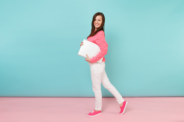 Full length portrait of woman in knitted rose sweater white pants holding laptop pc computer isolated on bright pink blue pastel wall background in studio. Fashion lifestyle concept Mock up copy space