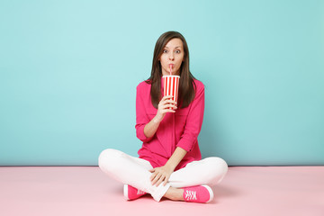 Full length portrait woman in rose shirt blouse white pants sitting on floor hold cup of soda isolated on bright pink blue pastel wall background studio. Fashion lifestyle concept. Mock up copy space.