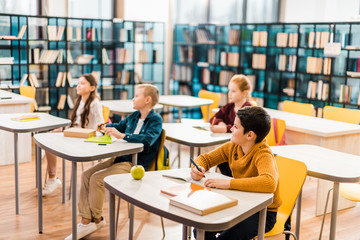 schoolchildren sitting at desks and looking away during lesson in library