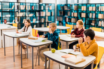 children sitting at desks and looking away during lesson in library