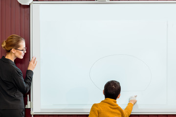 young teacher looking at schoolboy studying with interactive whiteboard