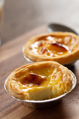 Egg tarts in aluminum foil cup on wood table,  traditional Portuguese dessert served in coffee shop