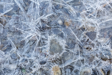 Frozen water in shallow water. Round stones among many sharp blue icicles
