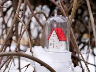 Naklejka premium Small toy decorative white house with a red roof and lighted illumination on a snow-covered tree, the concept of winter seasonal holidays, Christmas, a new home in the new year, home comfort