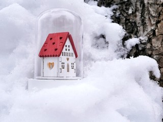 Small toy decorative white house with a red roof and lighted illumination on a snow-covered tree, the concept of winter seasonal holidays, Christmas, a new home in the new year, home comfort
