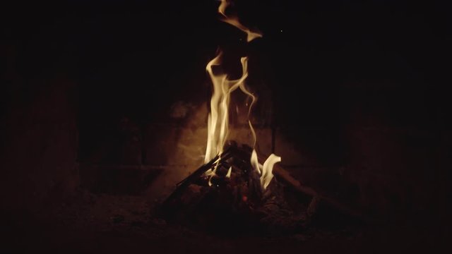 Flames dance over split log, illuminating brick backwall of fireplace