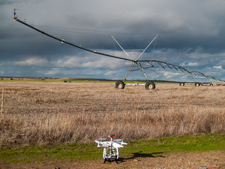 A drone next to a crop field with a pivot irrigation system in autumn on a cloudy day